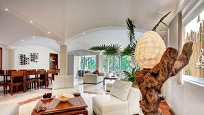 Een ruime woonkamer in modern design, met een grote houten sculptuur, een eethoek met houten stoelen en uitzicht op de omgeving door grote ramen.