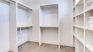 A walk-in closet with open shelving and a hanging rod, tiled floor, and white walls.
