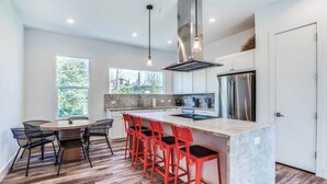 A modern kitchen with a central island, bar stools, a dining table, and a large window.