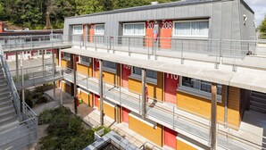 Un hotel de varios pisos con diseño moderno, que cuenta con balcones, un estacionamiento y vistas a una colina boscosa.
