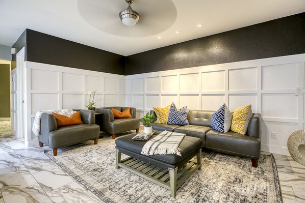 Una sala de estar con un sofá seccional, dos sillones, una mesa de centro y un tapete estampado.