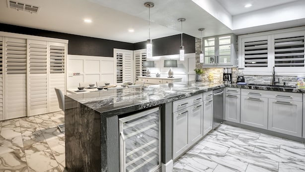 A modern kitchen with marble countertops, white cabinetry, and pendant lighting.