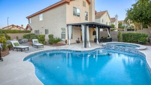 A swimming pool with a curved design, surrounded by lounge chairs and a covered patio area.