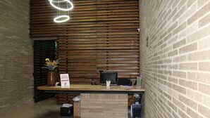 Un espace d’accueil avec un mur en lambris de bois, un comptoir d’accueil, un ordinateur et une plante en pot.