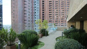 Un jardin sur le toit, agrémenté de plantes en pot, avec un espace aménagé pour s’asseoir, et des immeubles de grande hauteur en arrière-plan.