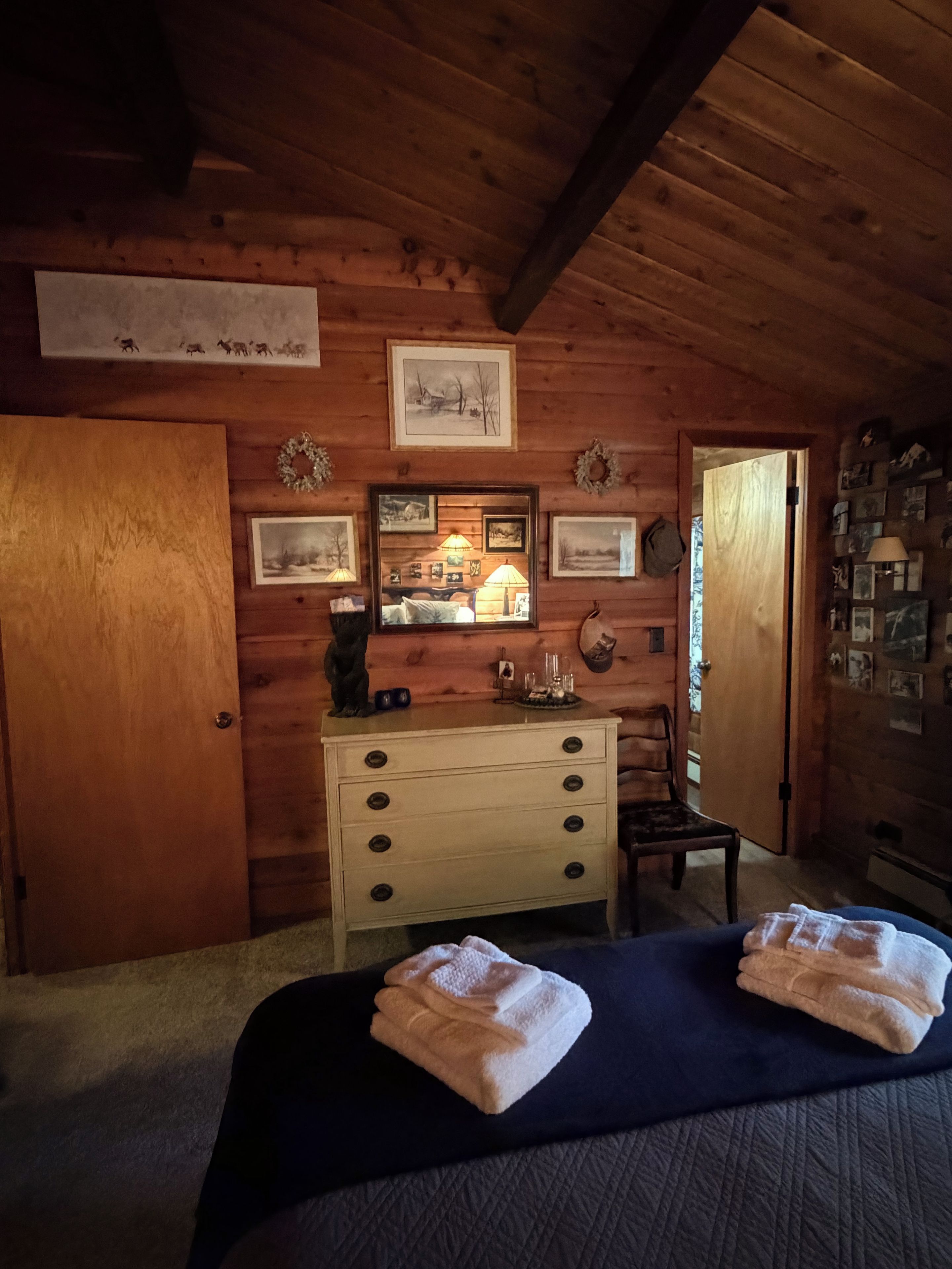A cozy cabin room with a bed, dresser, and wall-mounted pictures.