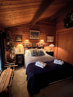 Un dormitorio de cabaña de madera acogedor con una cama, dos lámparas de noche, un cuadro enmarcado y un pequeño árbol de Navidad.