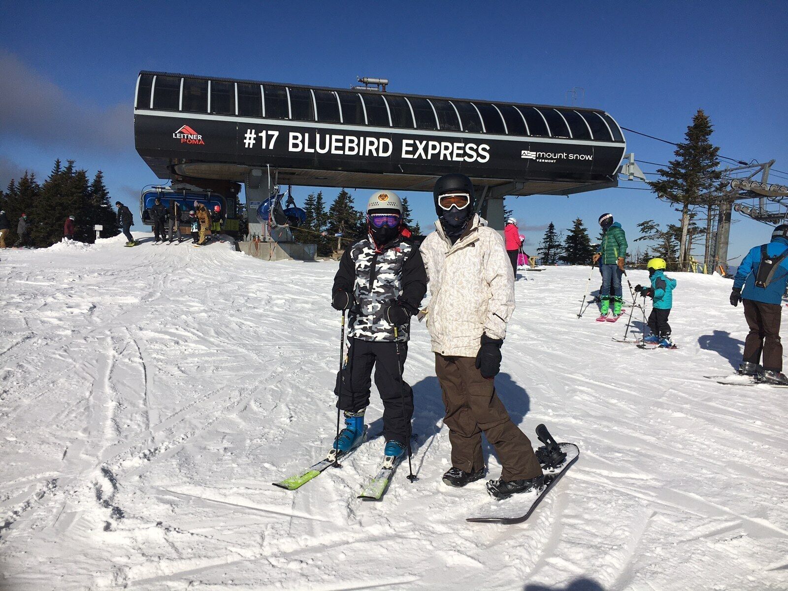 A ski lift with the sign '#17 BLUEBIRD EXPRESS' and a snowy slope with skiers and snowboarders.