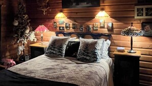 Un dormitorio rústico de cabaña con cama, dos lámparas de noche, un cuadro enmarcado en la pared y una mesita con lámpara.