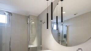 A modern bathroom with a glass shower enclosure, a large mirror, and a wooden vanity.