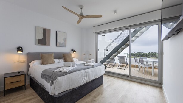 A modern bedroom with a large bed, a ceiling fan, and a view of a staircase leading to an outdoor area. - Ref. 396309 (Motril)