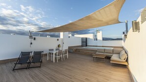 A rooftop terrace with a wooden deck, a sunshade, a pool, and outdoor seating.