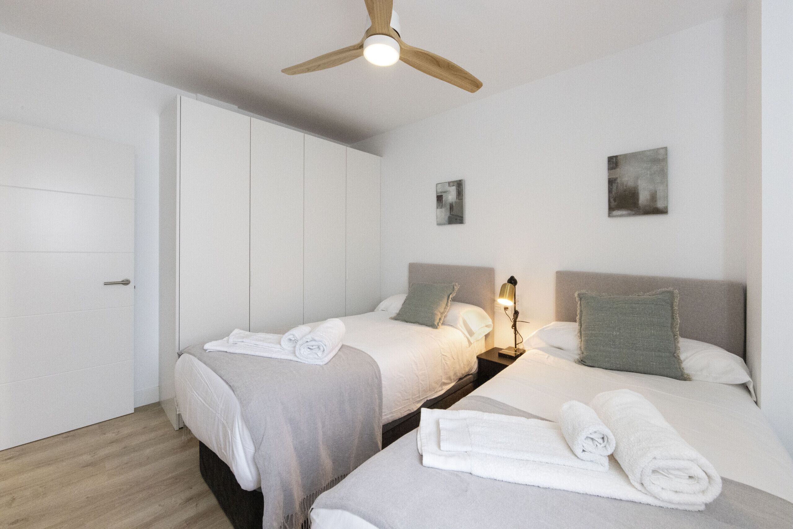 Een moderne hotelkamer met twee bedden, een plafondventilator en een nachtkastje met een lamp.