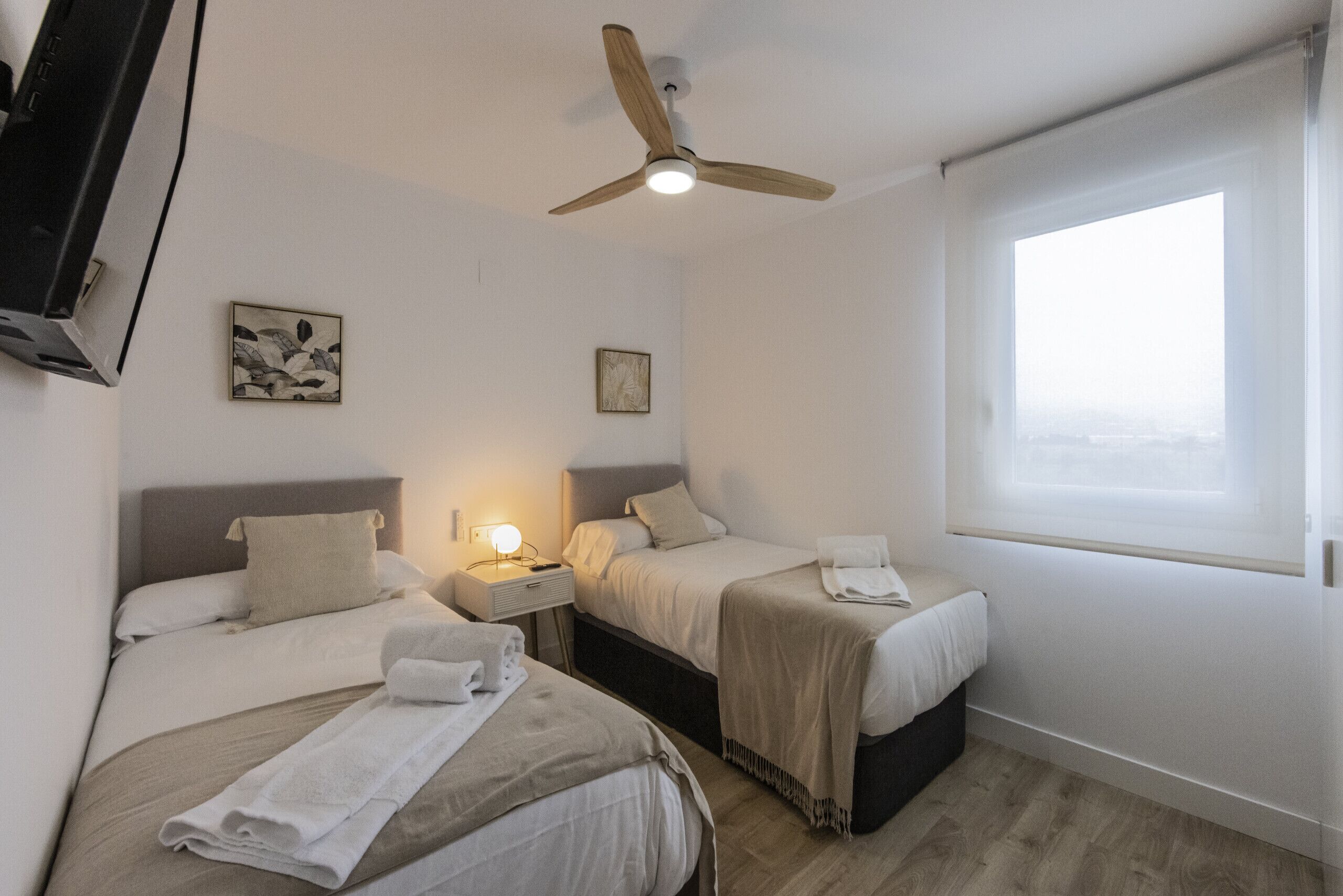 Habitación de hotel con dos camas, un ventilador de techo, una lámpara de noche y una ventana con vistas.