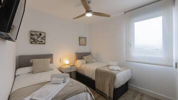Habitación de hotel con dos camas, un ventilador de techo, una lámpara de noche y una ventana con vistas.