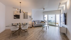 A modern living room with a glass dining table, white chairs, a grey sofa, and a flat-screen TV mounted on the wall. - Ref. 396309 (Motril)