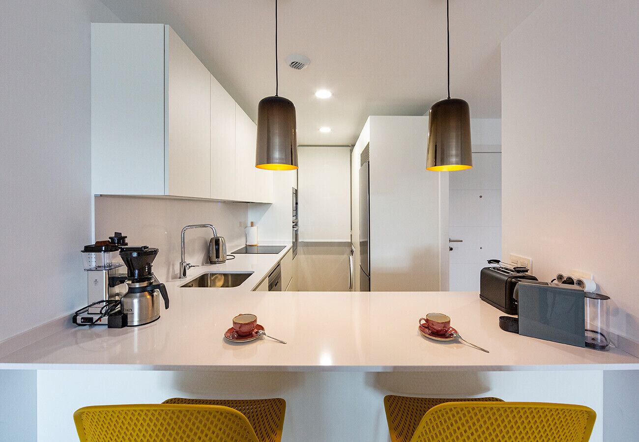 A modern kitchen with a white countertop, stainless steel appliances, and yellow chairs.