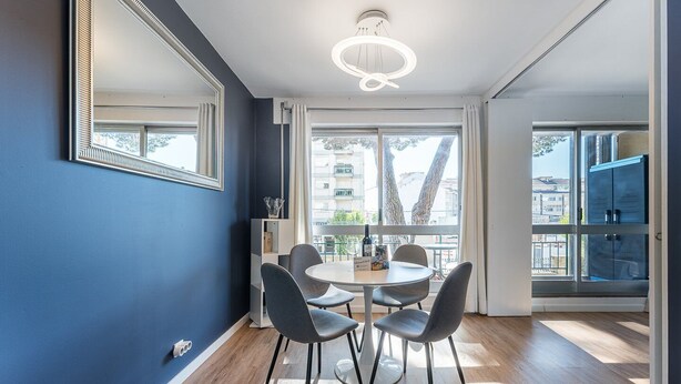 Ein stilvoller Essbereich mit einem runden Tisch, vier Stühlen, einem großen Spiegel und Blick durch große Fenster nach draußen.