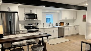 A modern kitchen with stainless steel appliances, white cabinets, and a wooden bar area with stools.