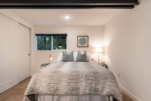 Une chambre à coucher avec un lit, deux tables de chevet, une fenêtre et un luminaire au plafond.