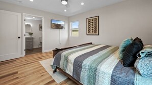 Une chambre à coucher comprenant un lit, un ventilateur de plafond, un éclairage encastré, une fenêtre et une porte donnant sur une salle de bain.