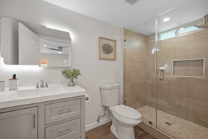 A modern bathroom with a white vanity, a toilet, and a glass-enclosed shower.