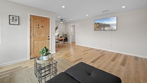 Un salon moderne avec un plancher en bois, un canapé foncé, une petite table sur laquelle est posée une plante, et un tableau accroché au mur.