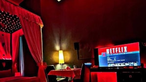 Una habitación con poca luz y ambiente rojo, que incluye un televisor mostrando el logotipo de Netflix, una mesa con sillas y un sofá.