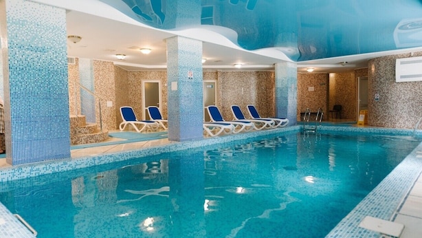 Una piscina interior con paredes y techo de azulejos azules, rodeada de sillones de descanso.