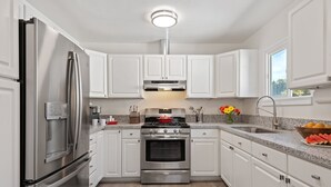A modern kitchen with white cabinets, stainless steel appliances, a granite countertop, and a window providing natural light.