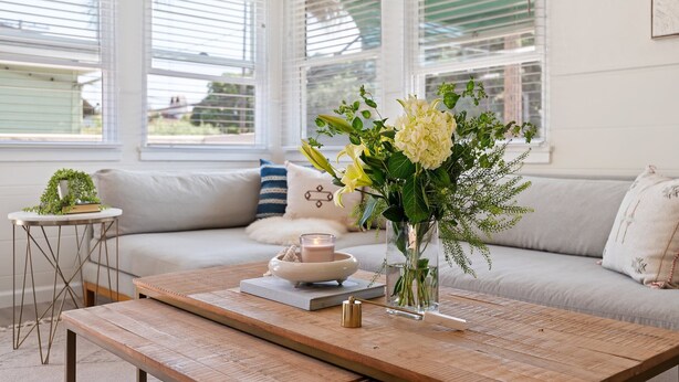 A cozy living room with a sofa, a coffee table, and a vase of flowers.