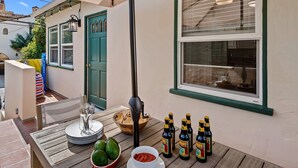 Eine Terrasse mit Tisch, gedeckt für eine Mahlzeit, darunter Teller, Schüsseln und Bierflaschen.