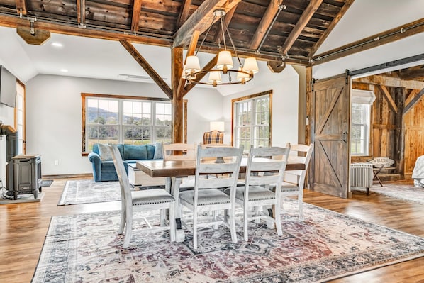 A rustic interior with a dining area featuring a wooden table and chairs, a blue sofa, and a large window offering a view of the outdoors.