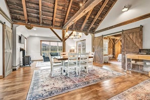 A spacious room with a wooden ceiling, a dining area with a table and chairs, a sofa, and a large window.