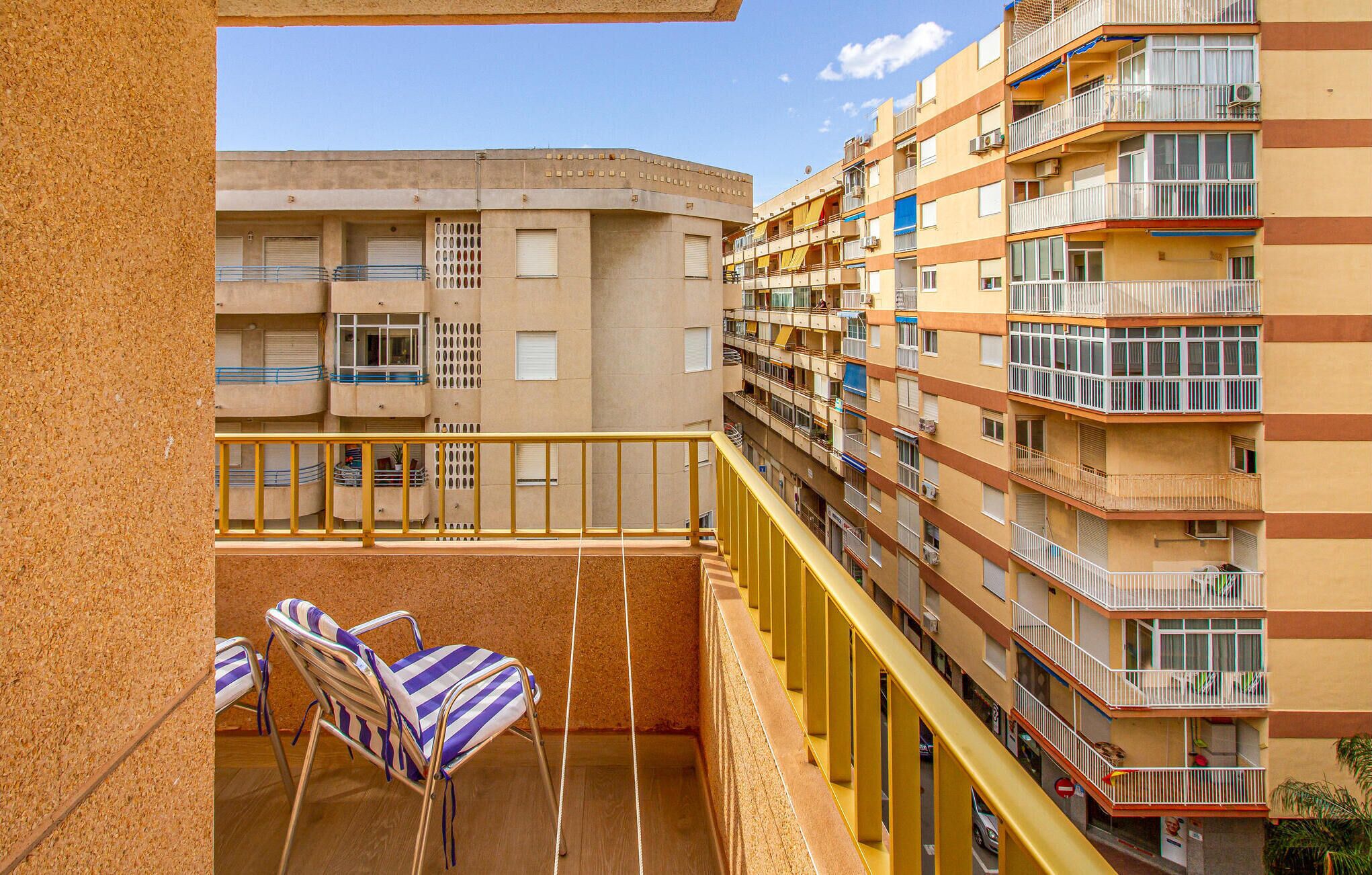 A multi-story residential building with balconies, a wooden floor, and striped chairs.
