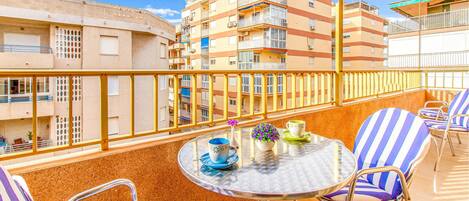 A balcony with a round table, striped chairs, and a view of multi-story buildings.