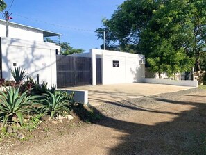 A modern building with a gated entrance, a paved driveway, and a landscaped area with plants.