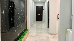Un couloir moderne avec un mur en marbre, une porte sombre au fond et un extincteur sur le côté droit.