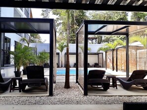 A covered outdoor seating area with lounge chairs and a pool in the background. - Whitestone Parkview Tamarindo 2 queen bed studio w/kitchen 7 min walk to beach (Tamarindo)