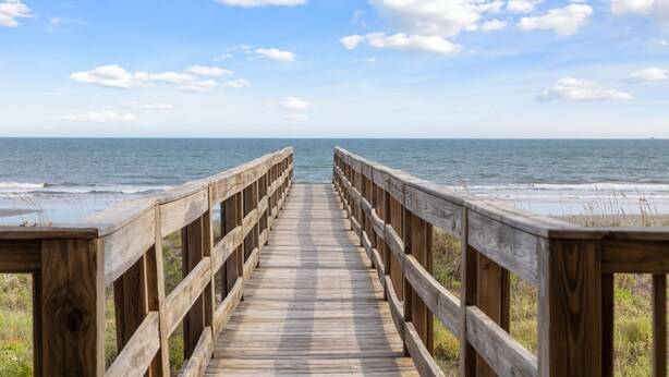 A wooden boardwalk leading to the beach with a clear sky and calm sea. - All Occasion House! Grand Oceanfront Home, Direct Beach Access, Large Ocean View Windows (Folly Beach)