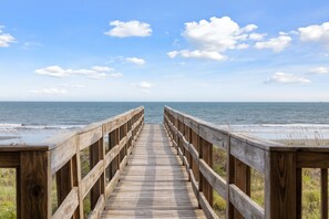 Een houten looppad dat naar het strand leidt, met een heldere lucht en een kalme zee.