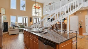 A spacious kitchen with a central island, a white staircase, and a large bay window. - All Occasion House! Grand Oceanfront Home, Direct Beach Access, Large Ocean View Windows (Folly Beach)