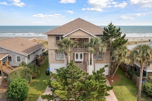 Une maison à deux étages avec un porche à l’avant, un petit jardin et une vue sur la plage.