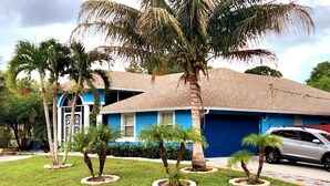 A residential house with a blue exterior, a garage, and a lawn with palm trees. - Beach like you've never seen! Heated pool/spa! (Port St. Lucie)