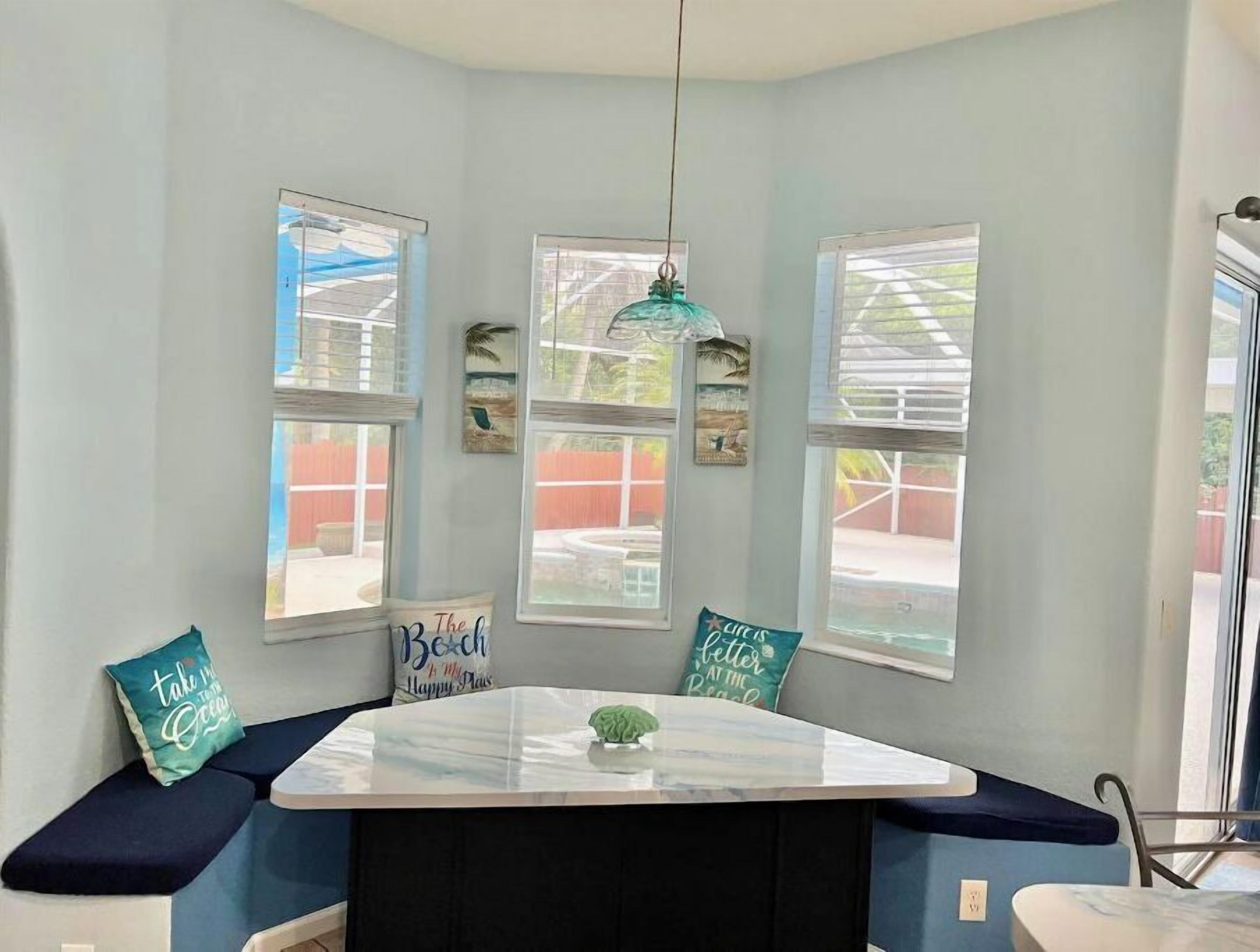 A room with a bay window, a table with a glass top, and a bench with cushions.