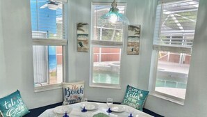 A dining area with a table set for four, surrounded by windows with beach-themed decor. - Beach like you've never seen! Heated pool/spa! (Port St. Lucie)