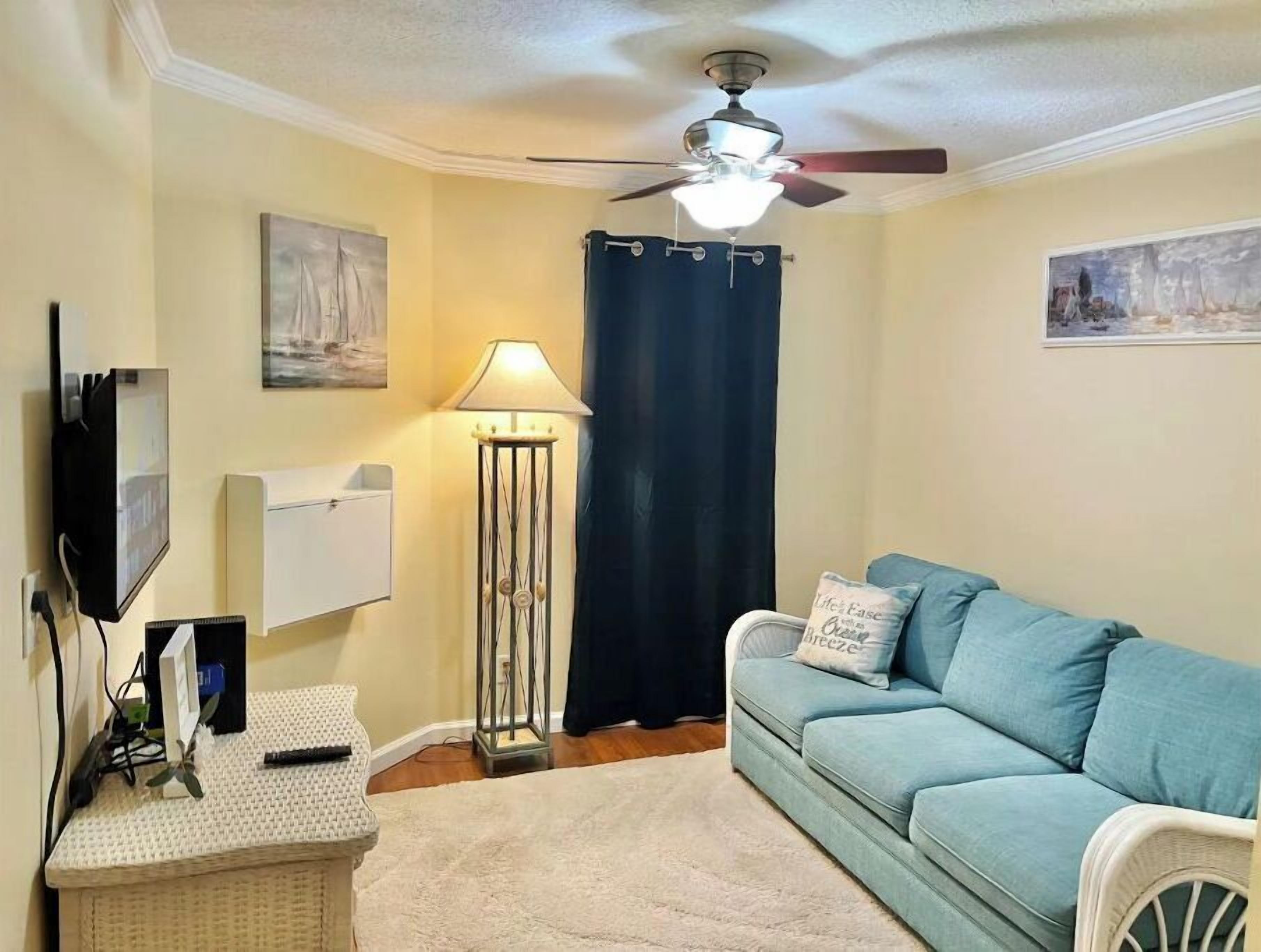 Un salon avec un ventilateur de plafond, une lampe sur pied, un téléviseur, un canapé et un tapis.