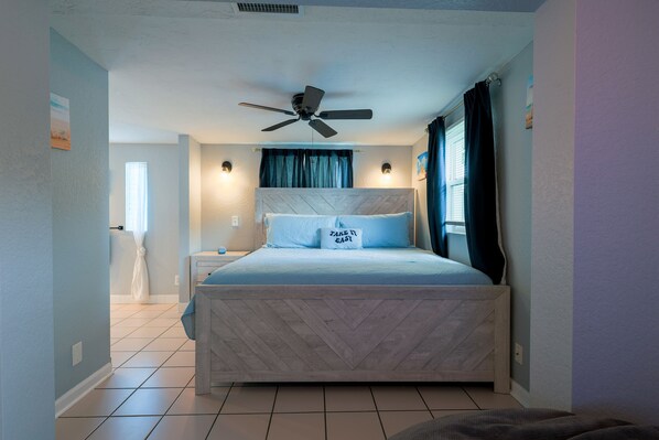 Quarto com cama, ventilador de teto e mesa de cabeceira.