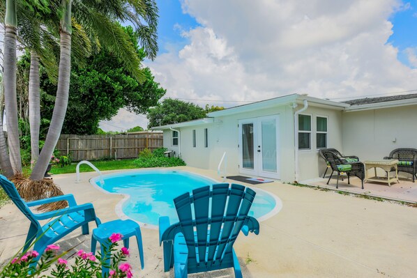 A backyard with a swimming pool, blue chairs, and a small table.