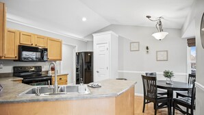 Una cocina con armarios de madera, encimera de granito, pileta de acero inoxidable y comedor con mesa y sillas.